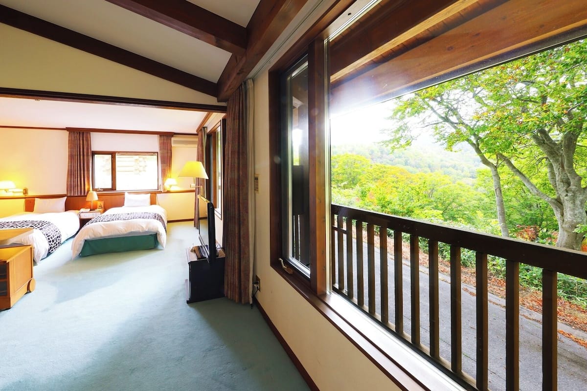 Ein Hotelzimmer mit zwei Betten, einem Balkon mit Geländer und Blick auf Grünflächen.