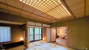 Una habitación japonesa tradicional con suelo de tatami, futón, puertas correderas y vistas a un jardín.