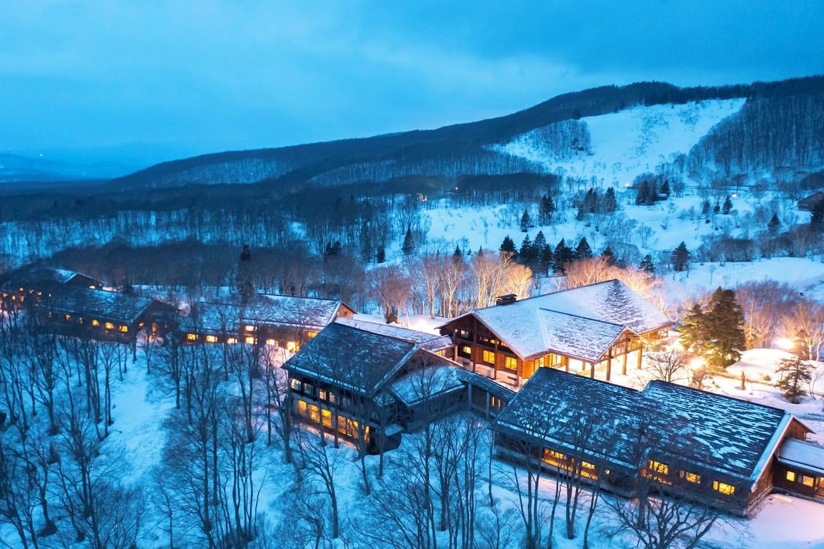 Ein mit Schnee bedecktes Chalet mit mehreren Hütten, umgeben von Bäumen und Bergen.