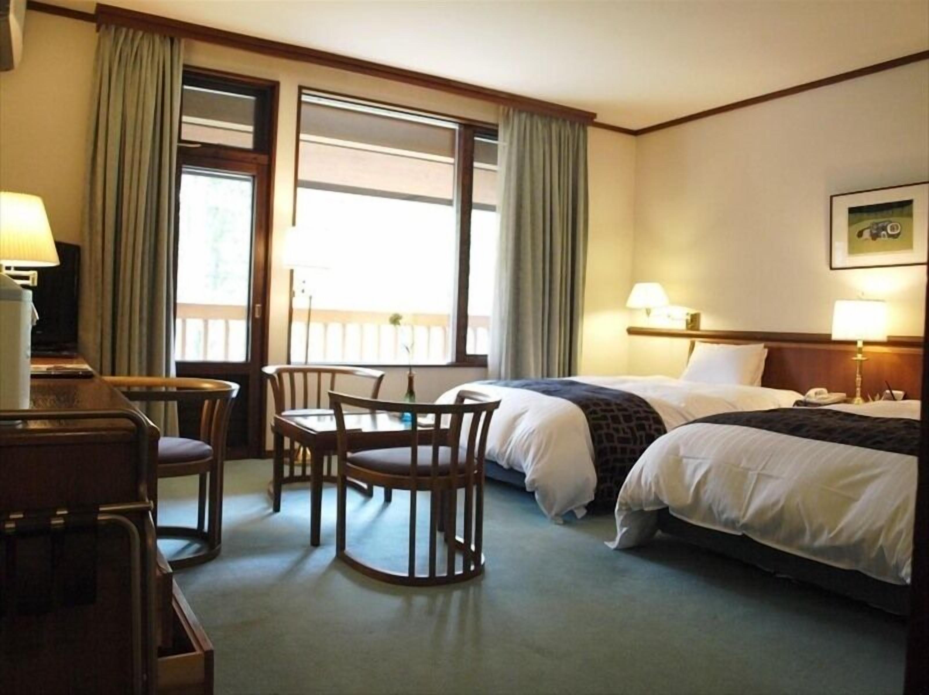 Una habitación de hotel con cama, escritorio, dos sillas, mesa y ventana con cortinas.