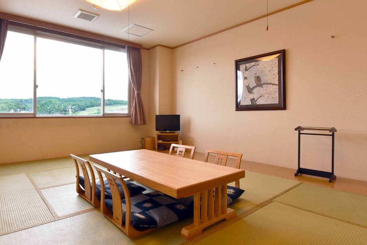 A room with tatami mats, a wooden table, chairs, a television, and a framed picture on the wall.