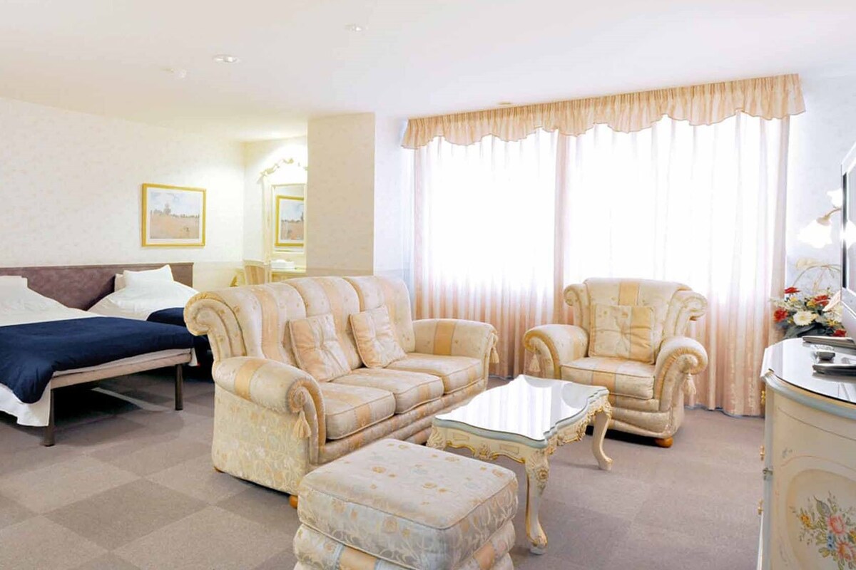 Una habitación de hotel con una cama, dos sofás, una mesa de centro y una mesita auxiliar.