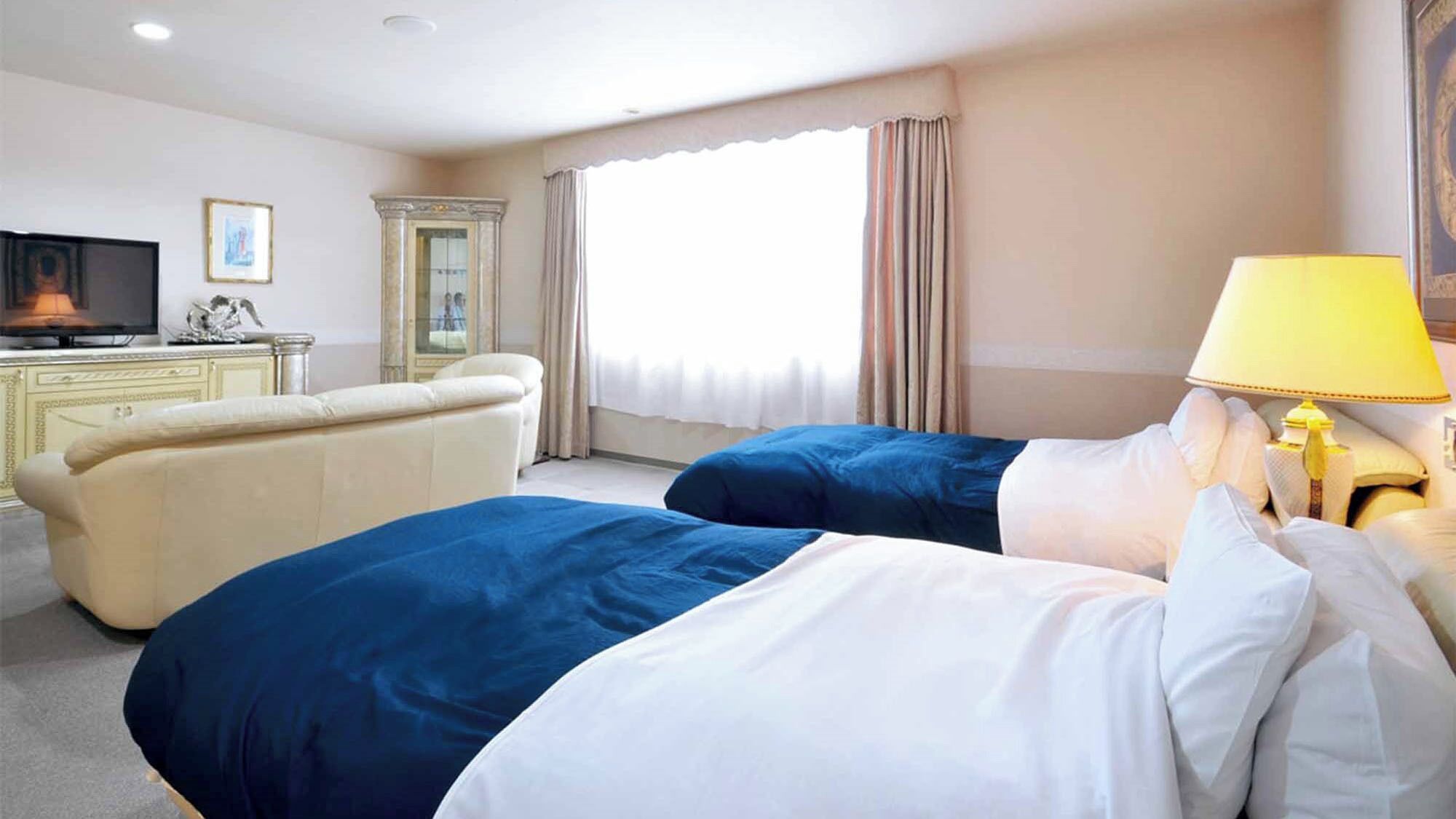 A hotel room with two beds, a television, a desk, and a window with curtains.