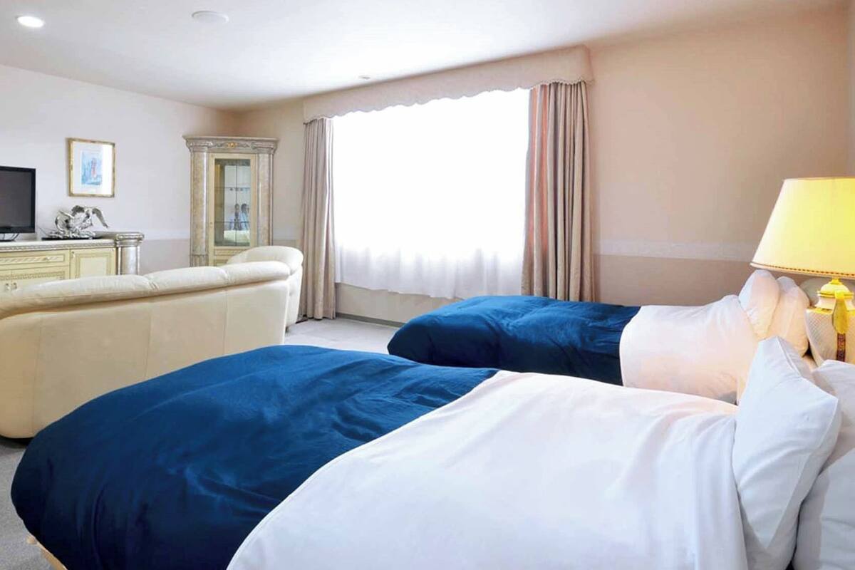 A hotel room with two beds, a television, a desk, and a window with curtains.