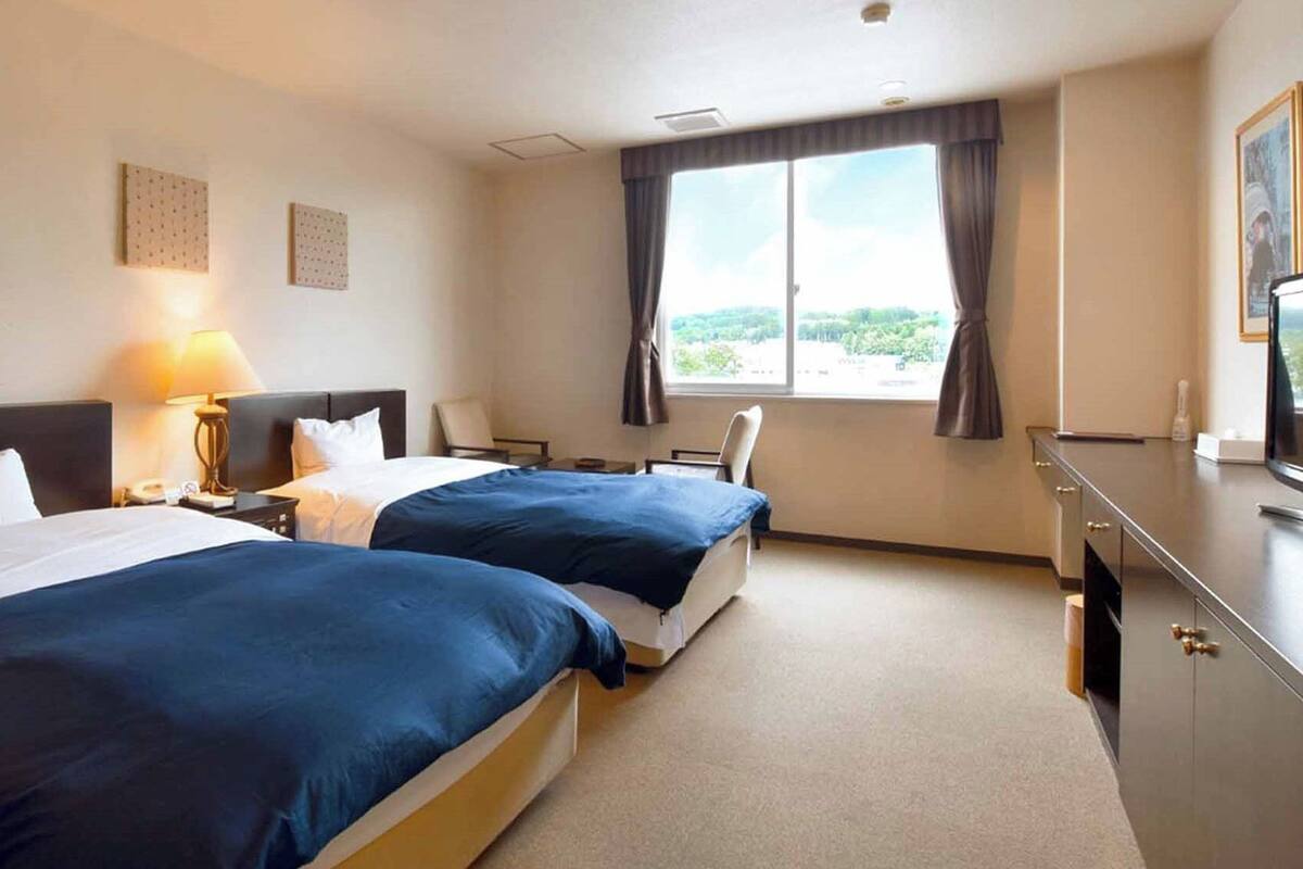 A hotel room with two beds, a desk, a chair, a TV, and a window with a view.