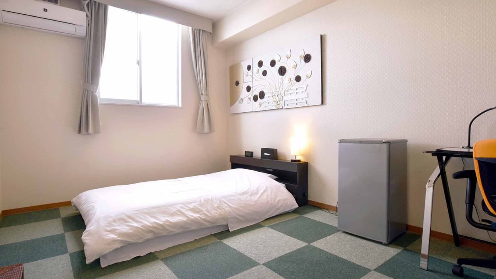 Une chambre d’hôtel équipée d’un lit, d’un bureau, d’une chaise, d’un réfrigérateur et d’une œuvre d’art accrochée au mur.