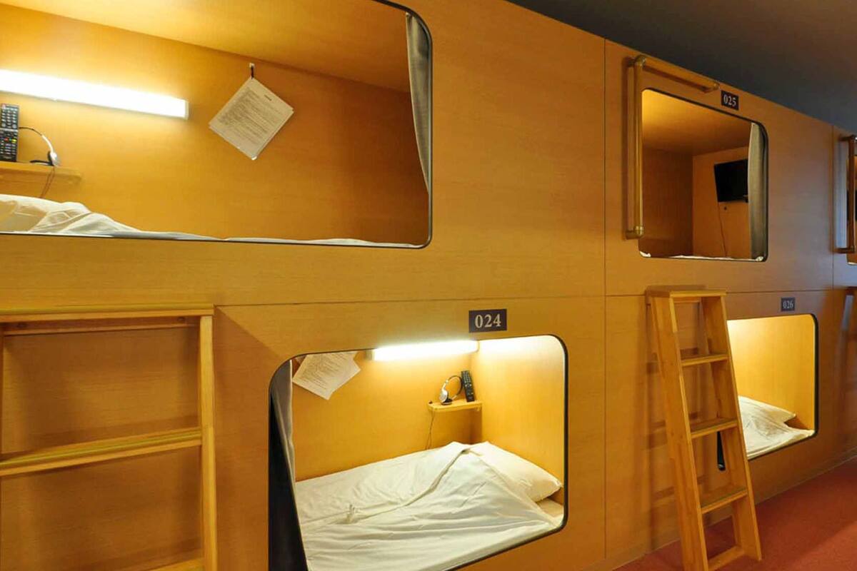 A row of single beds with wooden frames, each with a small bedside table, a mirror, and a light.
