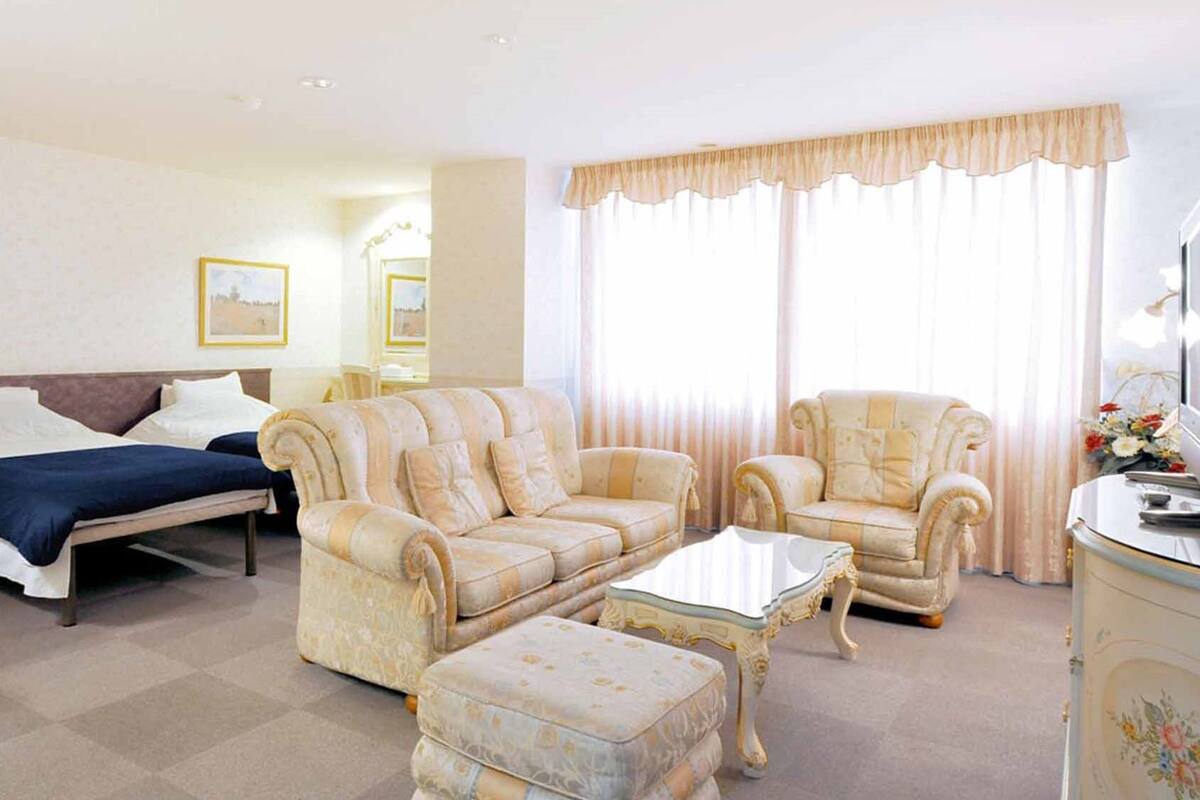 A hotel room with a bed, two sofas, a coffee table, and a side table.