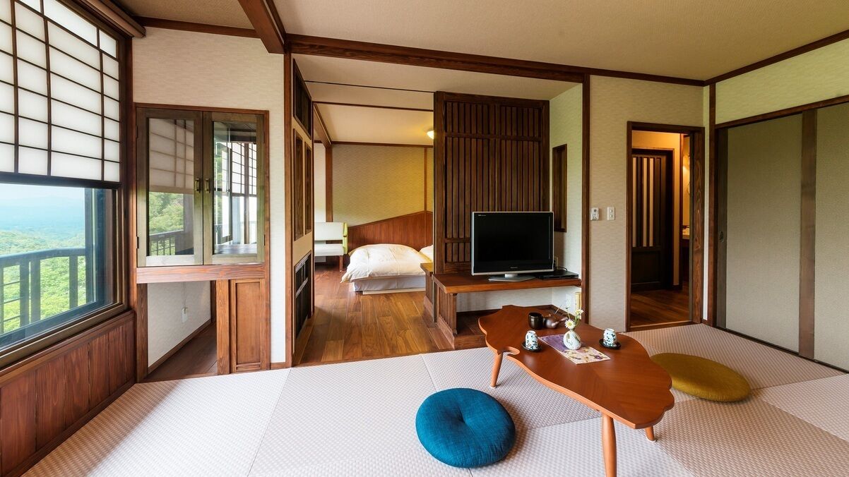 Una habitación de estilo japonés tradicional con suelo de tatami, una cama, un televisor y vistas al exterior.