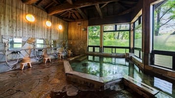 A stone-floored spa area with wooden walls, a large window, and a hot tub.