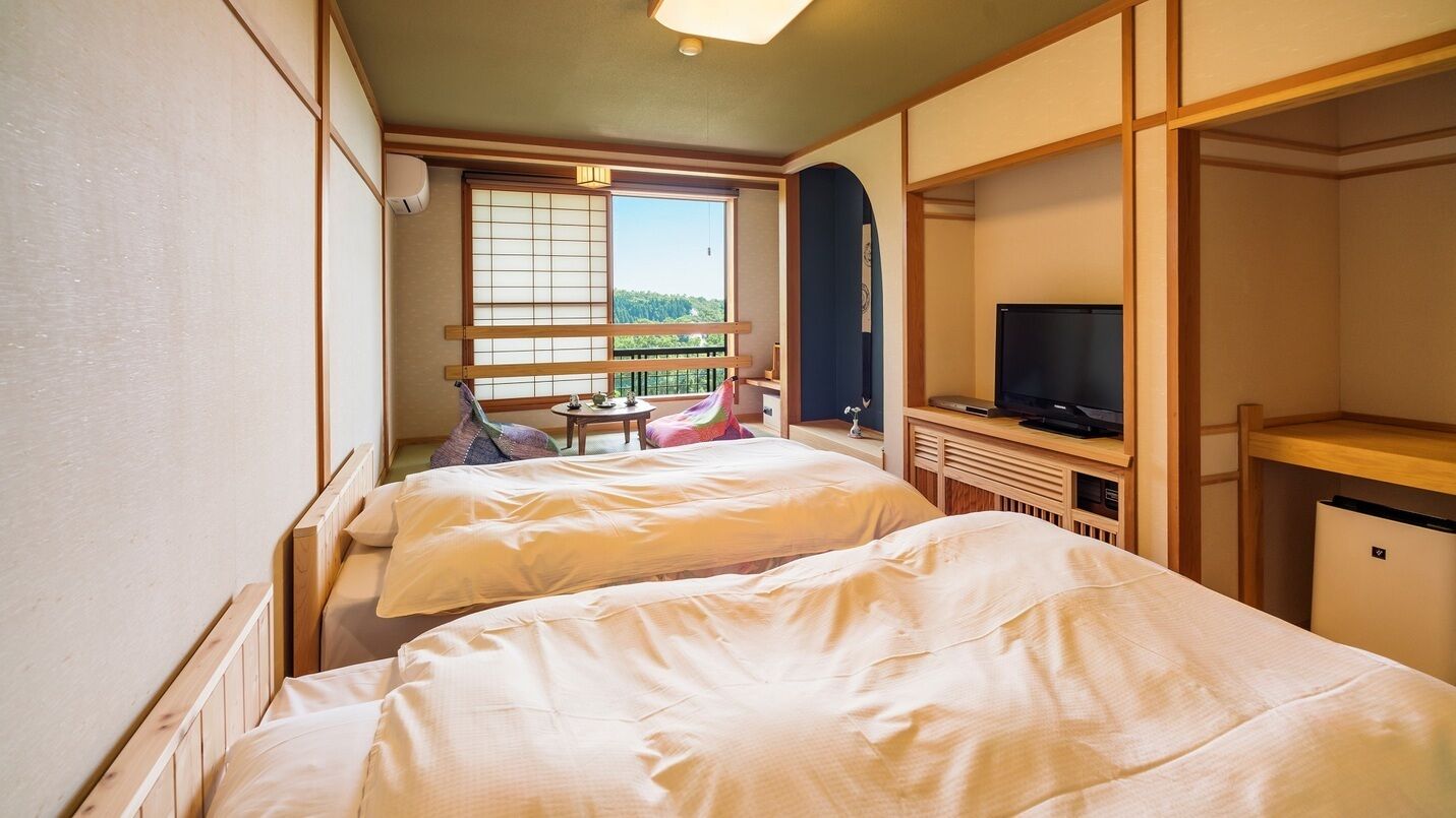 Habitación de hotel con dos camas, un televisor, una mesita con tetera y vistas al exterior.