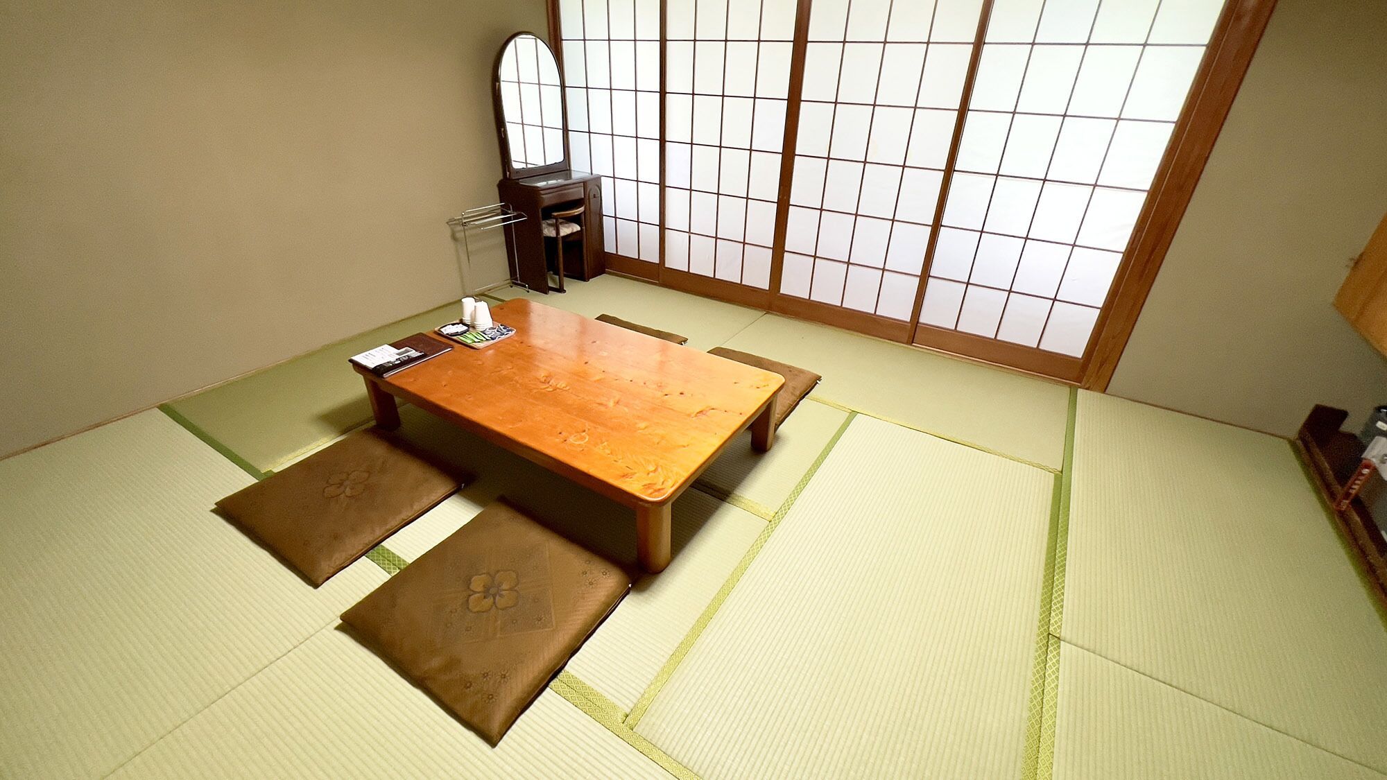 A tatami mat room with a low wooden table, cushions, and a shoji screen.