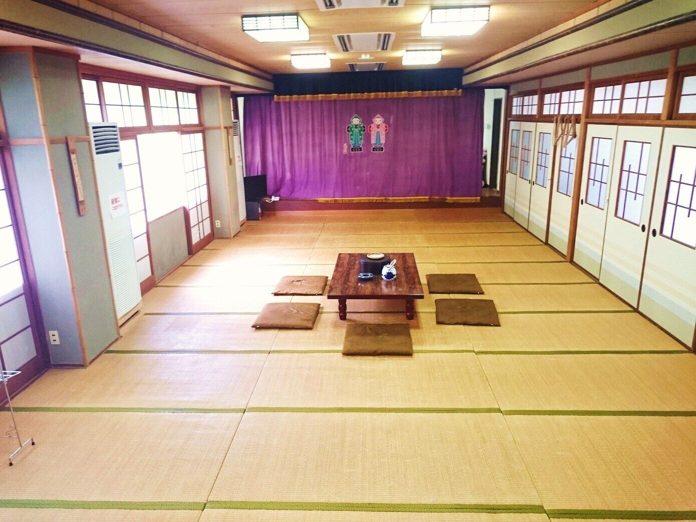 A traditional Japanese room with tatami flooring, a wooden table, and a purple curtain backdrop.