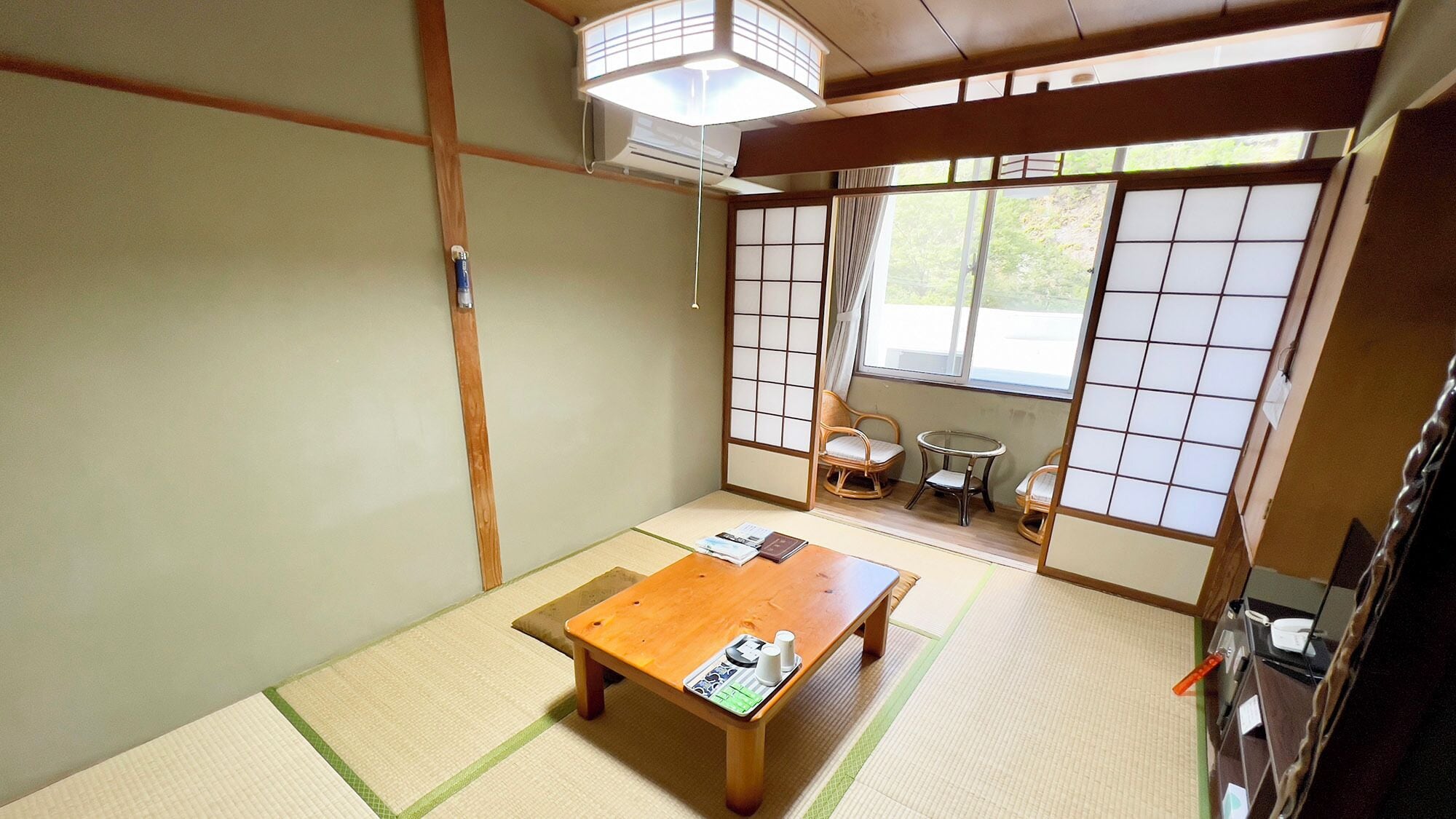 A traditional Japanese room with tatami flooring, a wooden table, sliding shoji doors, and a view of the outdoors.