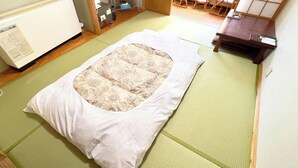 Ein Futonbett mit einer blumengemusterten Matratze, einem weißen Kopfkissen und einem grünen Tatami-Boden.