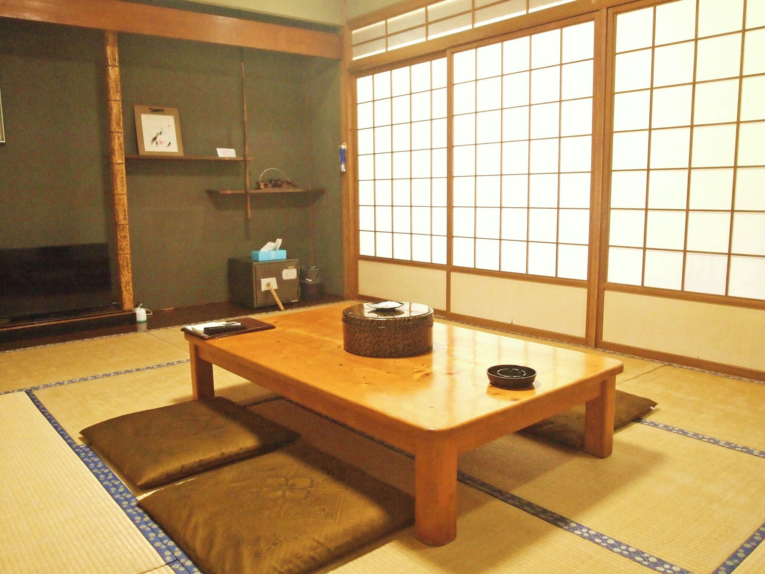 A tatami mat room with a wooden table, cushions, a television, and a shoji screen.