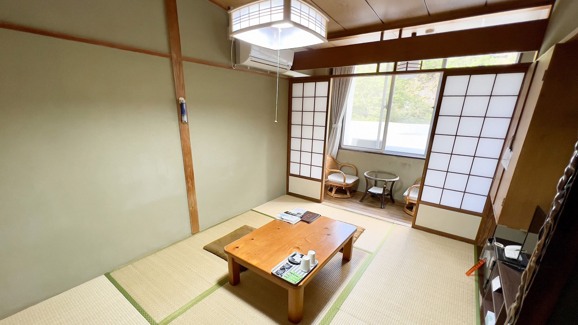 A traditional Japanese room with tatami flooring, a wooden table, a sliding door, and a view of the outside.