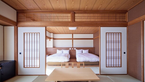 A traditional Japanese room with tatami flooring, a low wooden bed with white bedding, a wooden table, and sliding doors with shoji screens.