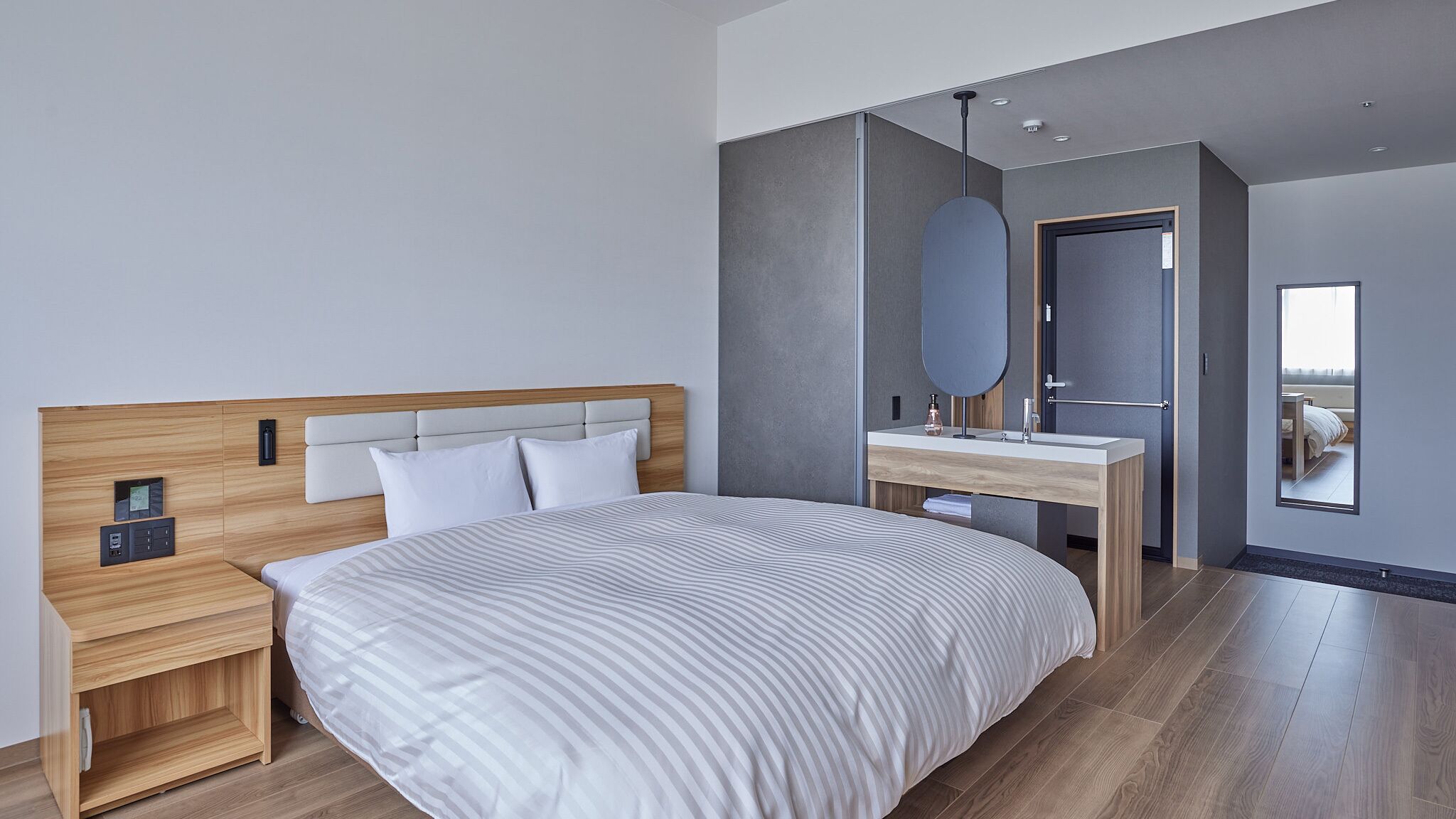 Quarto moderno com cama grande, mesa de cabeceira de madeira, um aparador, espelho e guarda-roupa embutido.