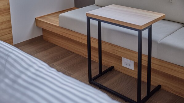 A modern room with a bed, a wooden bedside table, and a light-colored sofa.