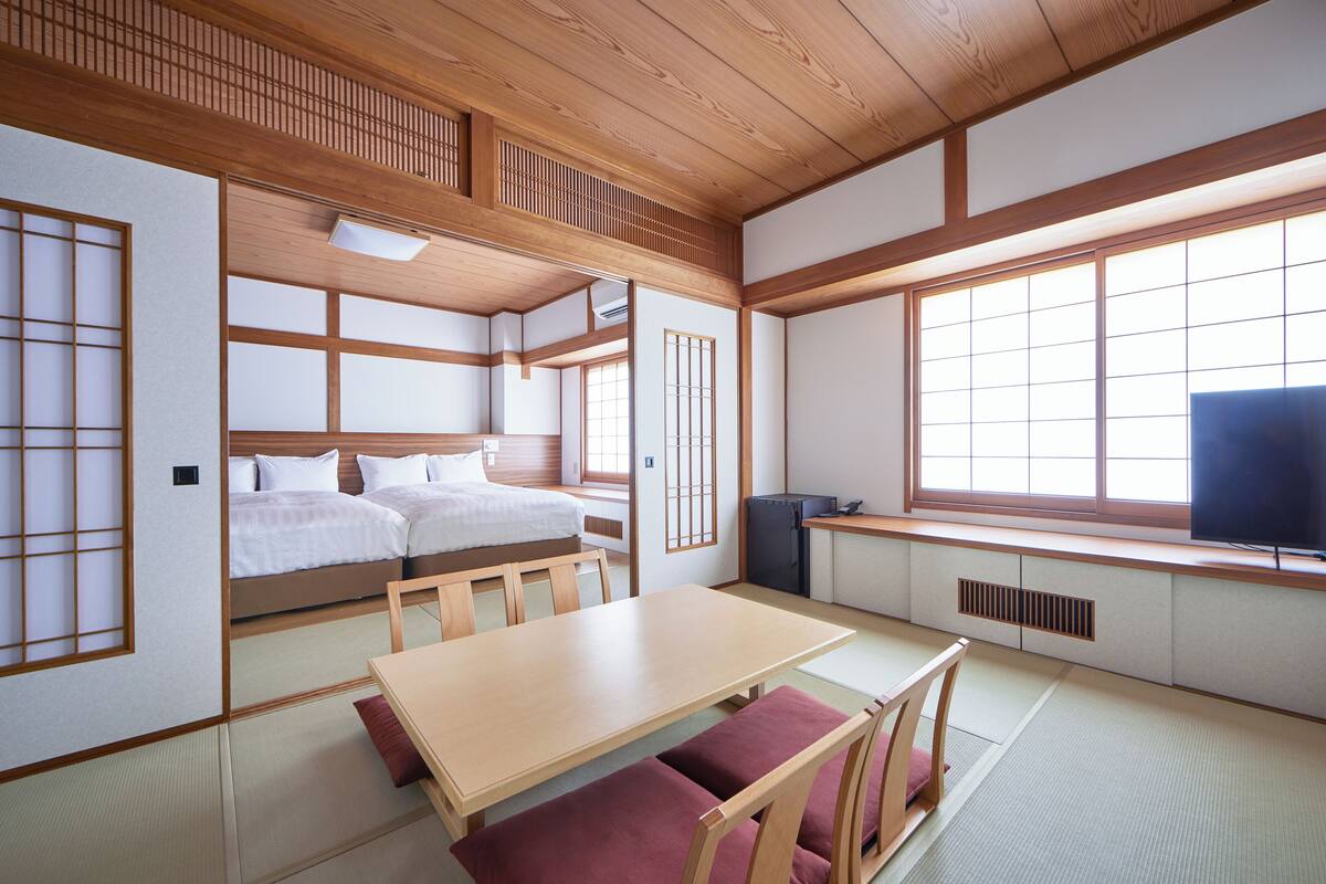 A traditional Japanese-style room with tatami flooring, a low wooden table, a bed with futon mattresses, and sliding doors.
