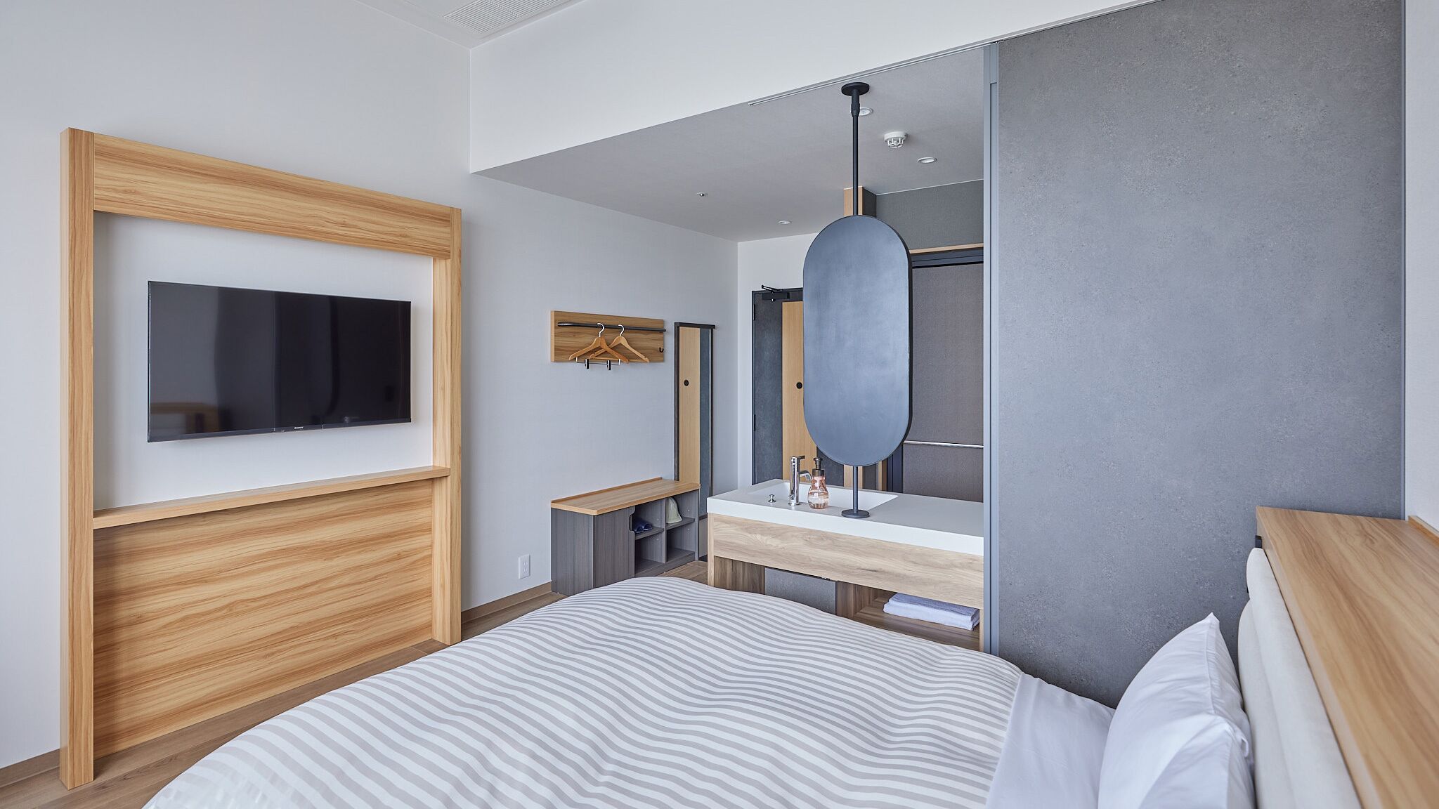 Une chambre moderne avec un grand lit, un téléviseur fixé au mur, une coiffeuse avec un miroir et un luminaire suspendu.