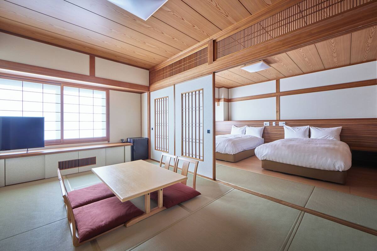 A traditional Japanese-style room with tatami flooring, a low table with cushions, a bed with white bedding, and sliding doors with wooden frames.