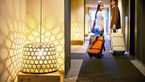 A hotel corridor with a decorative hanging light fixture and luggage in the background.
