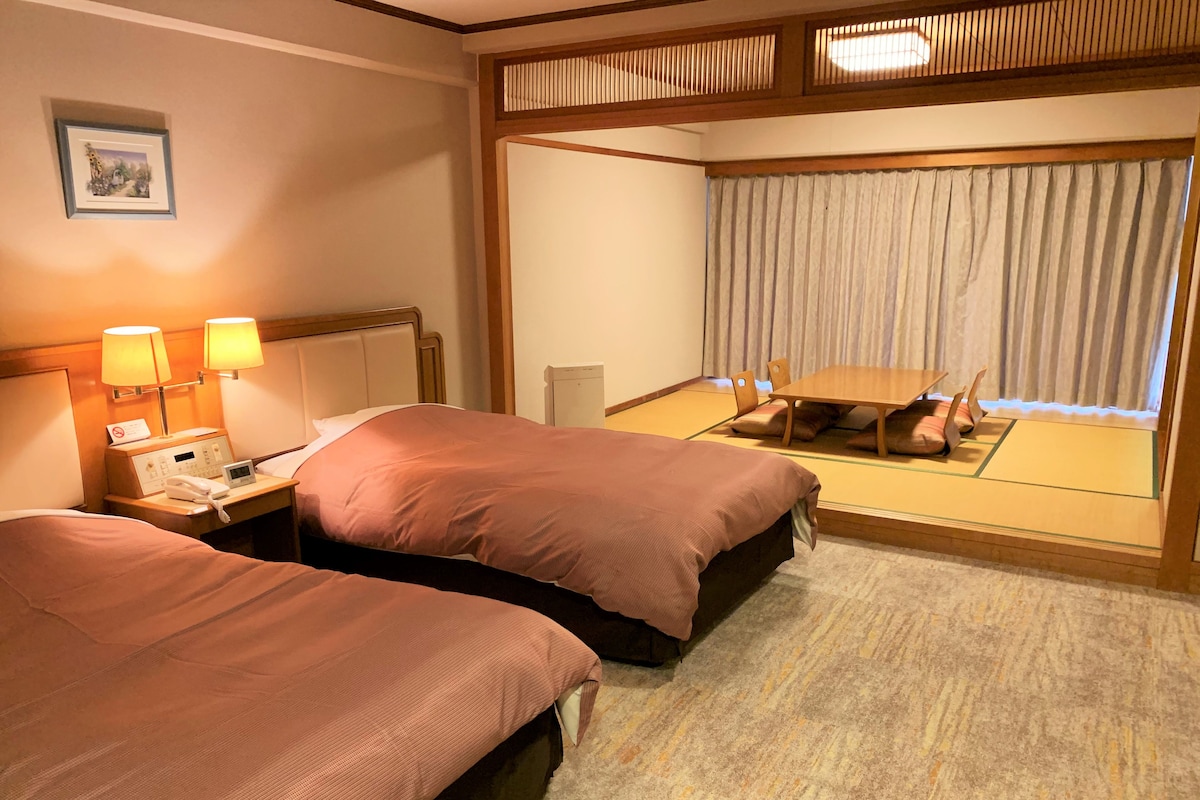 A hotel room with two beds, a bedside table with a phone, lamps, and a picture on the wall.