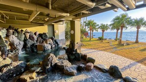 A rock garden with a water feature, a stone pathway, and palm trees by the sea. - Daikoku Resort Hotel (Shibushi)