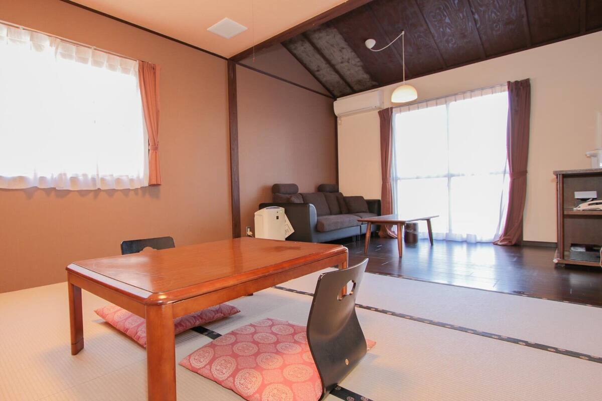 A traditional Japanese room with tatami flooring, a wooden table, a sofa, and a futon bed.