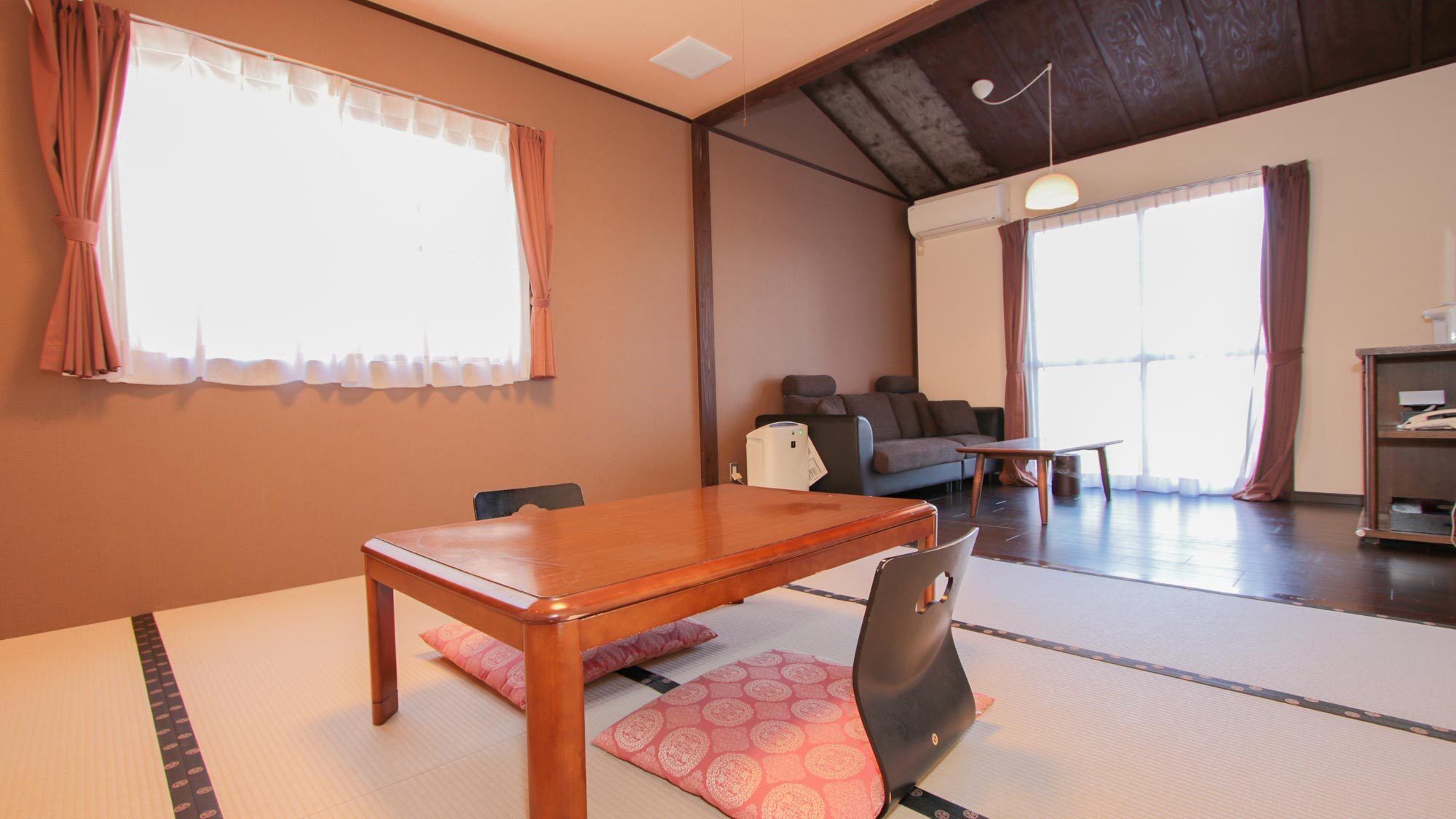 A room with a wooden table, tatami mat flooring, a sofa, and a desk with a lamp.