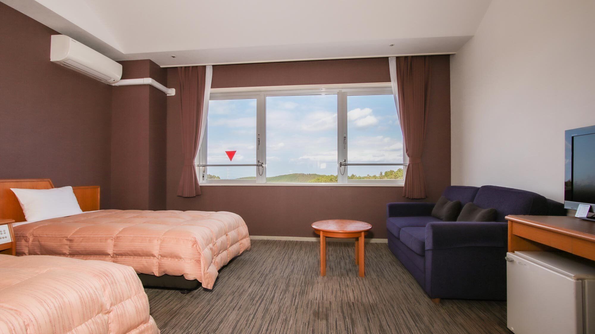 A hotel room with two beds, a sofa, a TV, a small table, and a window with a view.