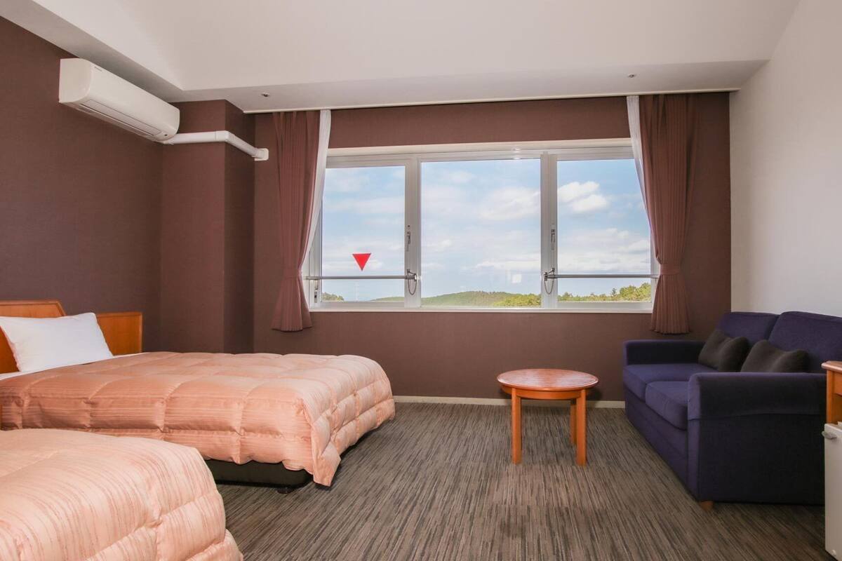 A hotel room with two beds, a sofa, a TV, a small table, and a window with a view.
