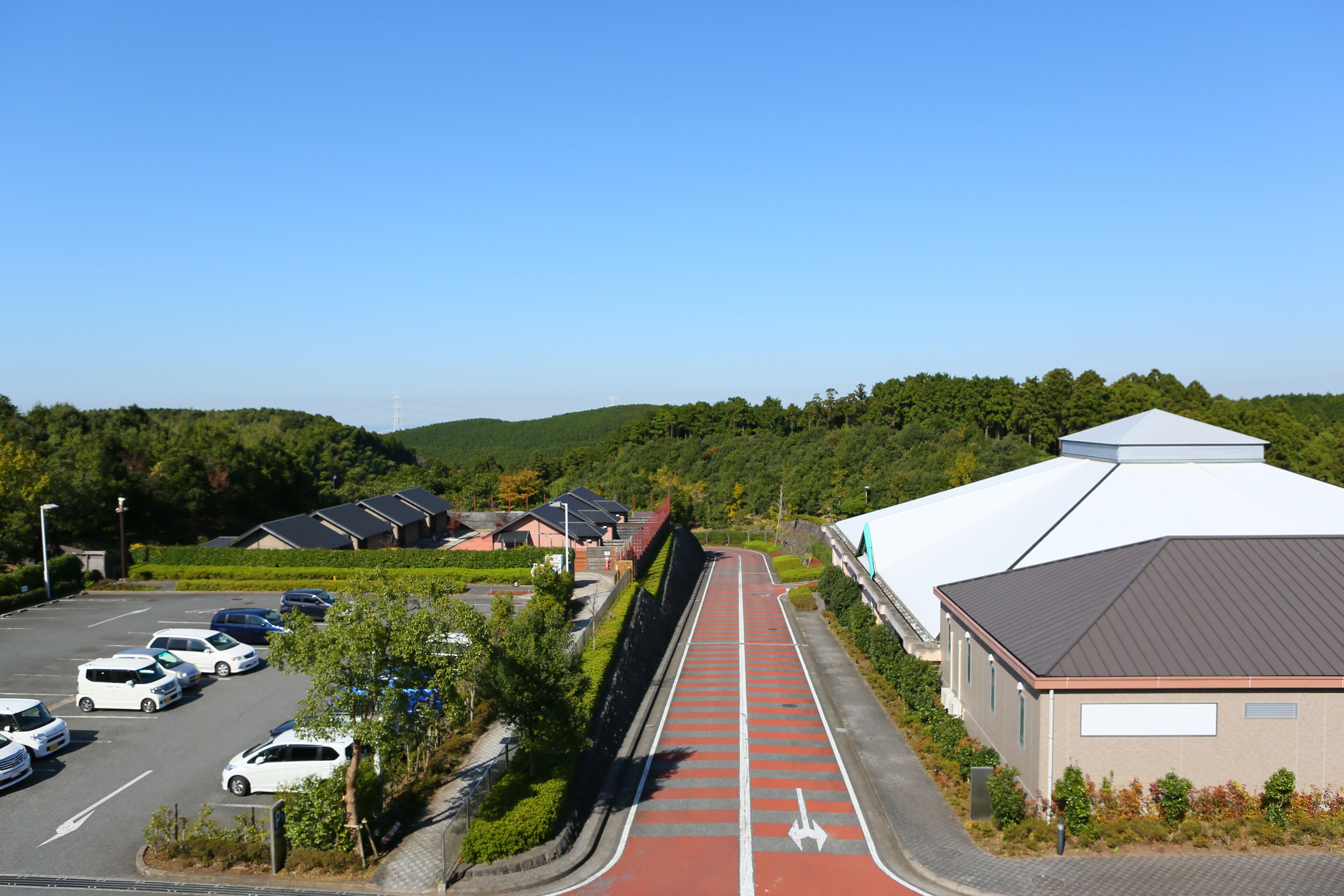 Ein Parkplatz mit Autos, ein roter Fahrradweg und ein Gebäude mit weißem Dach.