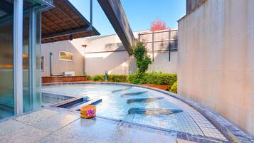 A modern outdoor swimming pool area with a covered seating area and a stone-tiled deck.
