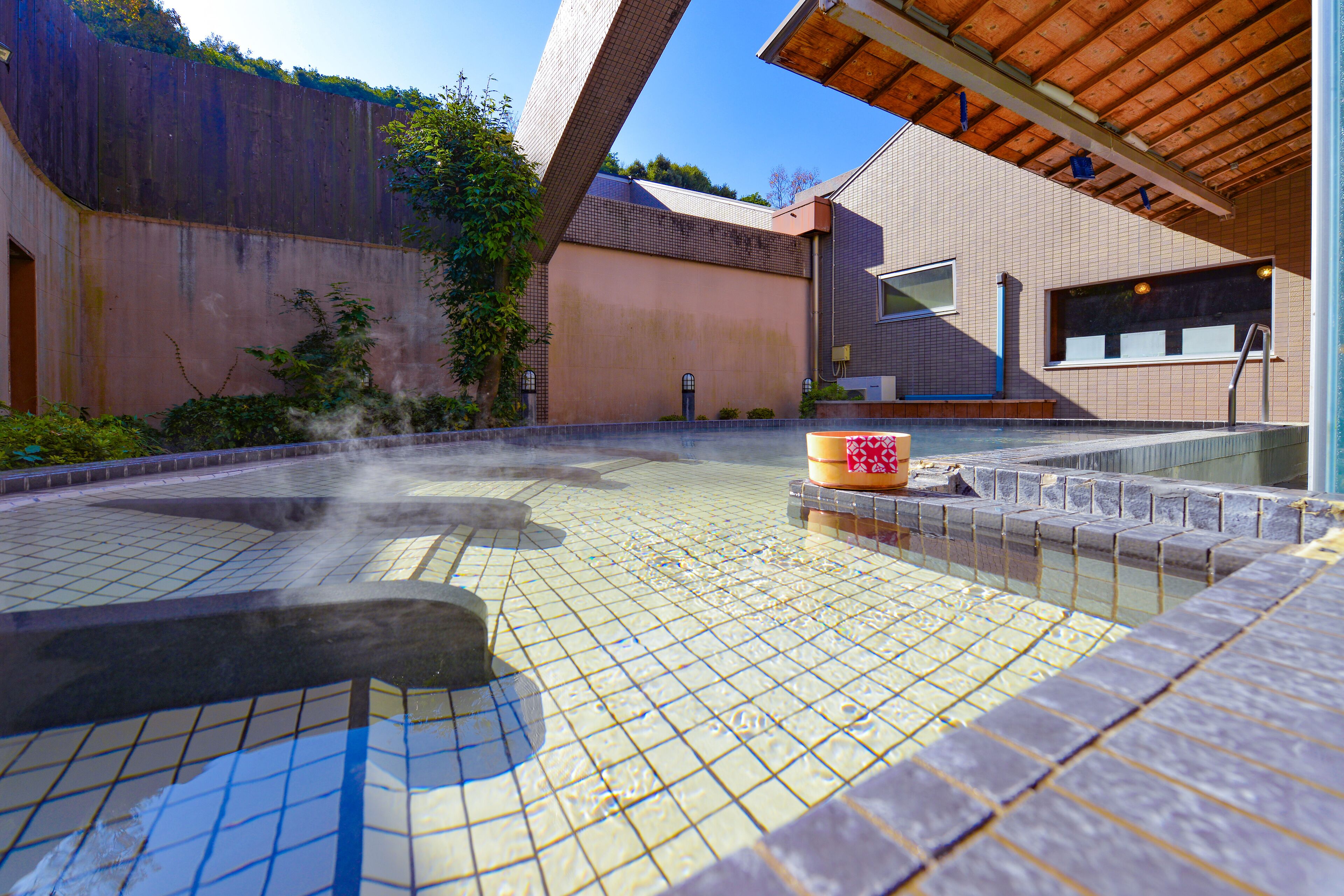 A hot spring area with tiled flooring, a wooden structure, and a building with large windows.