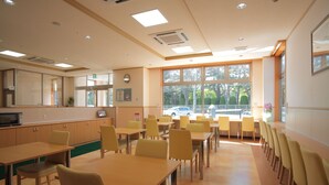 Un espace repas avec des tables et des chaises, un four à micro-ondes et une fenêtre donnant sur des arbres et une voiture.