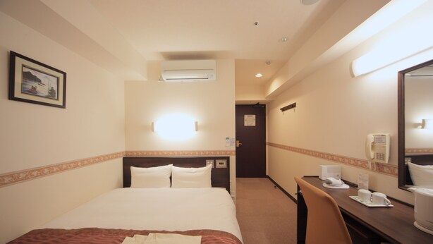 Une chambre d’hôtel équipée d’un lit, d’un bureau, d’une chaise, d’un téléphone et d’un miroir.