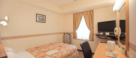 A hotel room with a bed, a desk with a computer, a chair, a television, and a window with curtains.