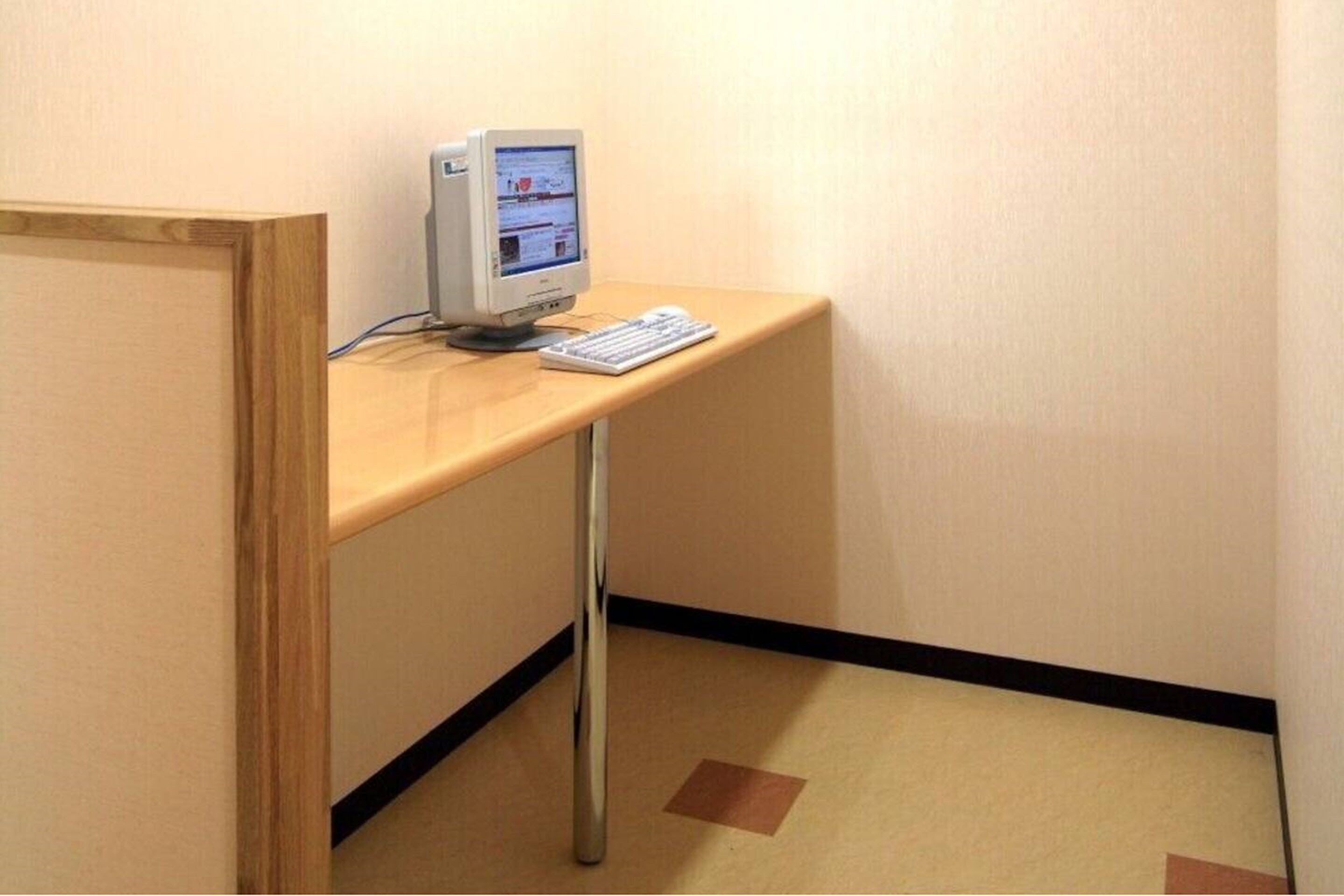 A corner desk with a computer and keyboard, a wooden partition, and a carpeted floor.