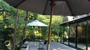 An outdoor patio with wooden tables and benches, surrounded by glass walls and a large umbrella. - Hakone Kuoritei (Hakone)
