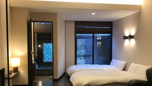 A modern hotel room with a large bed, a seating area with a sofa and a small table, and a view of trees through the window. - Hakone Kuoritei (Hakone)