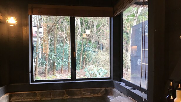 A stone bathtub with a view of a forest through large windows. - Hakone Kuoritei (Hakone)