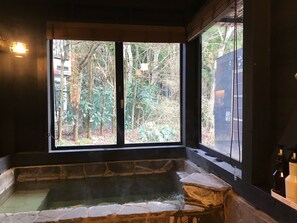 A stone bathtub with a view of a forest through large windows. - Hakone Kuoritei (Hakone)