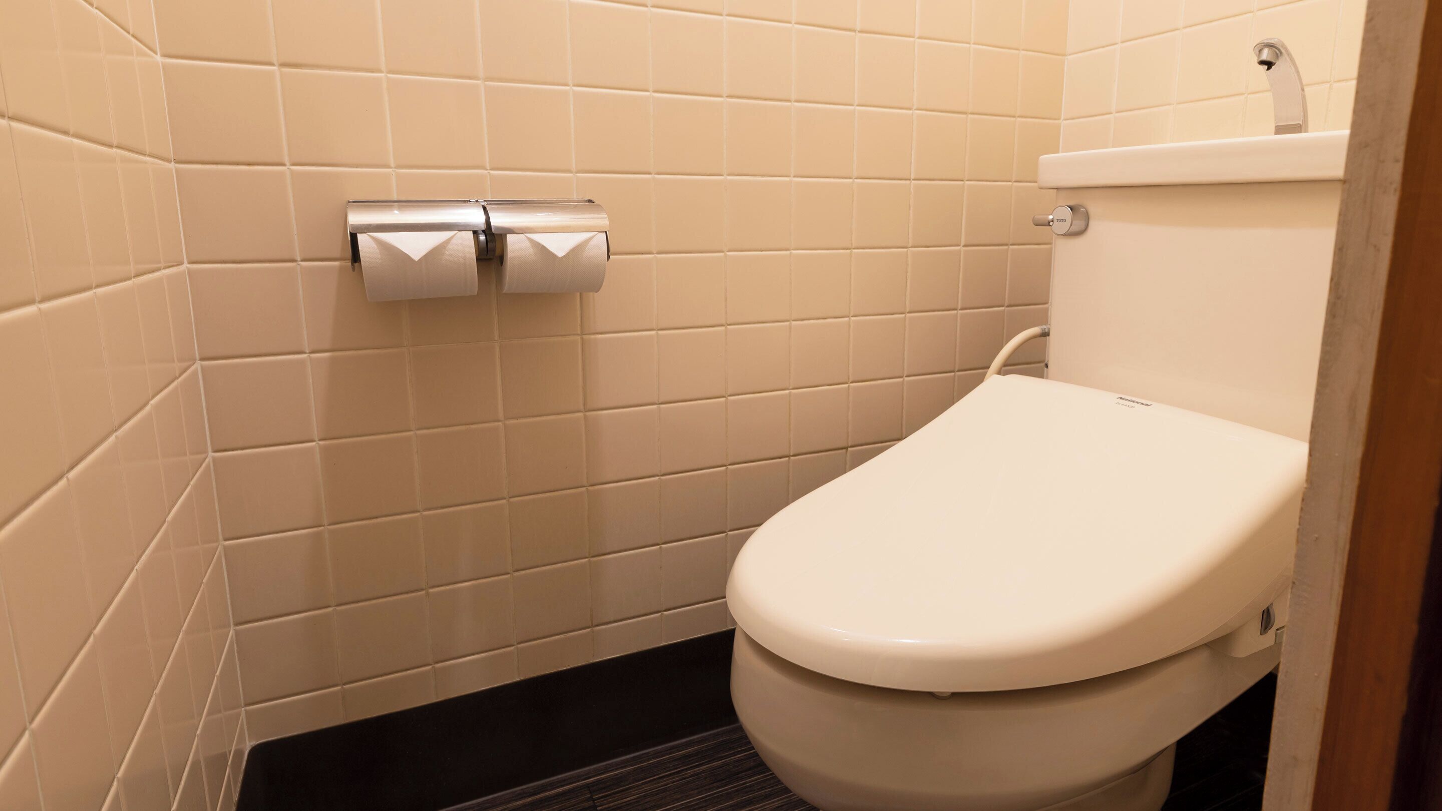 A small, modern bathroom with a toilet, a toilet paper holder, and a tiled wall.