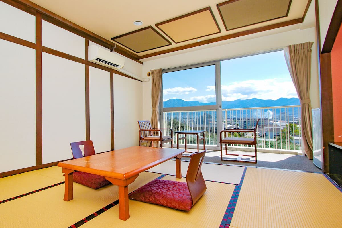 A traditional Japanese room with tatami flooring, a wooden table, and chairs, a large window with a mountain view.