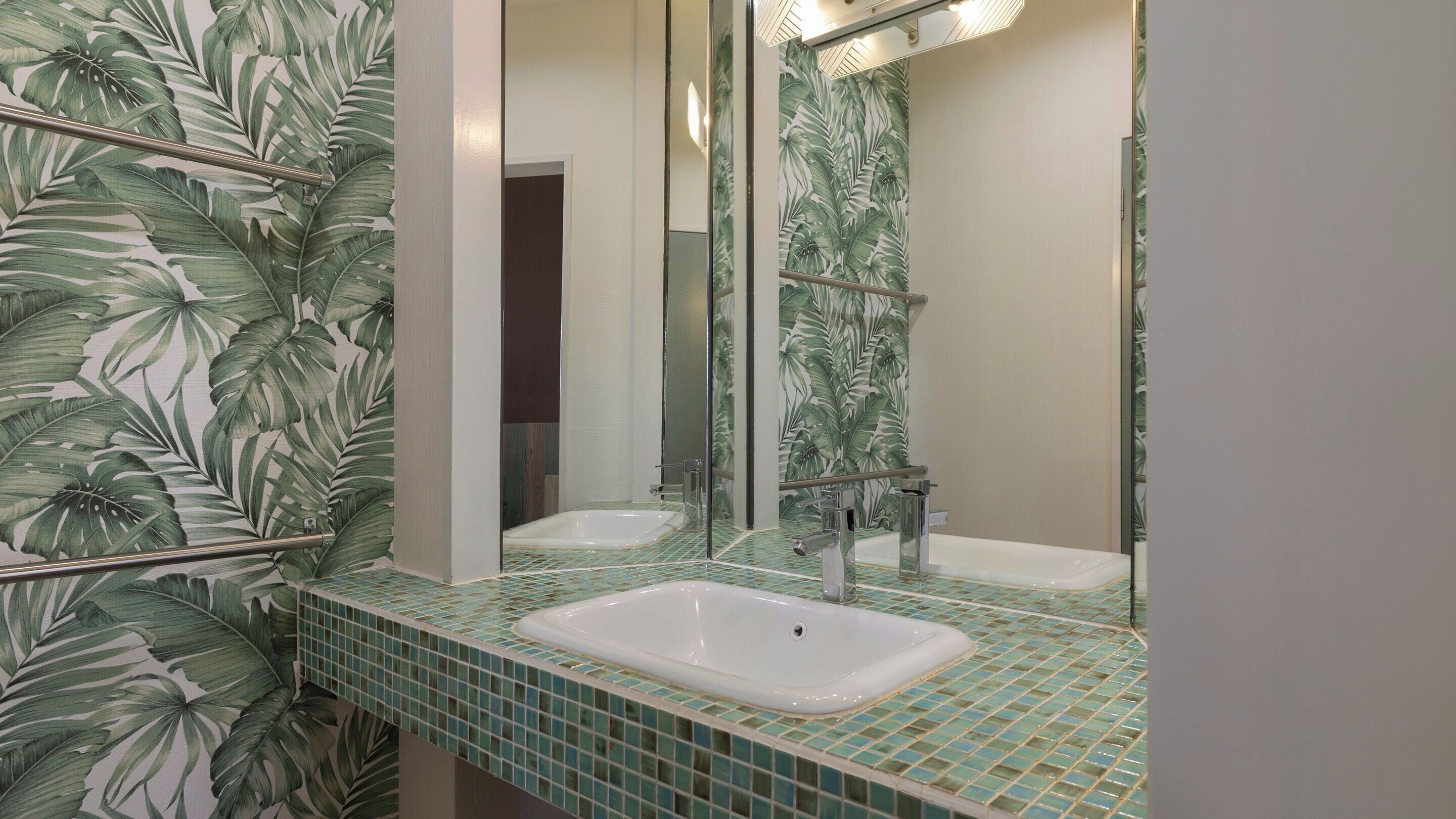 Une salle de bain dotée d’un grand miroir, de deux lavabos et d’un pare-feu en carreaux décoré d’un motif de feuilles.