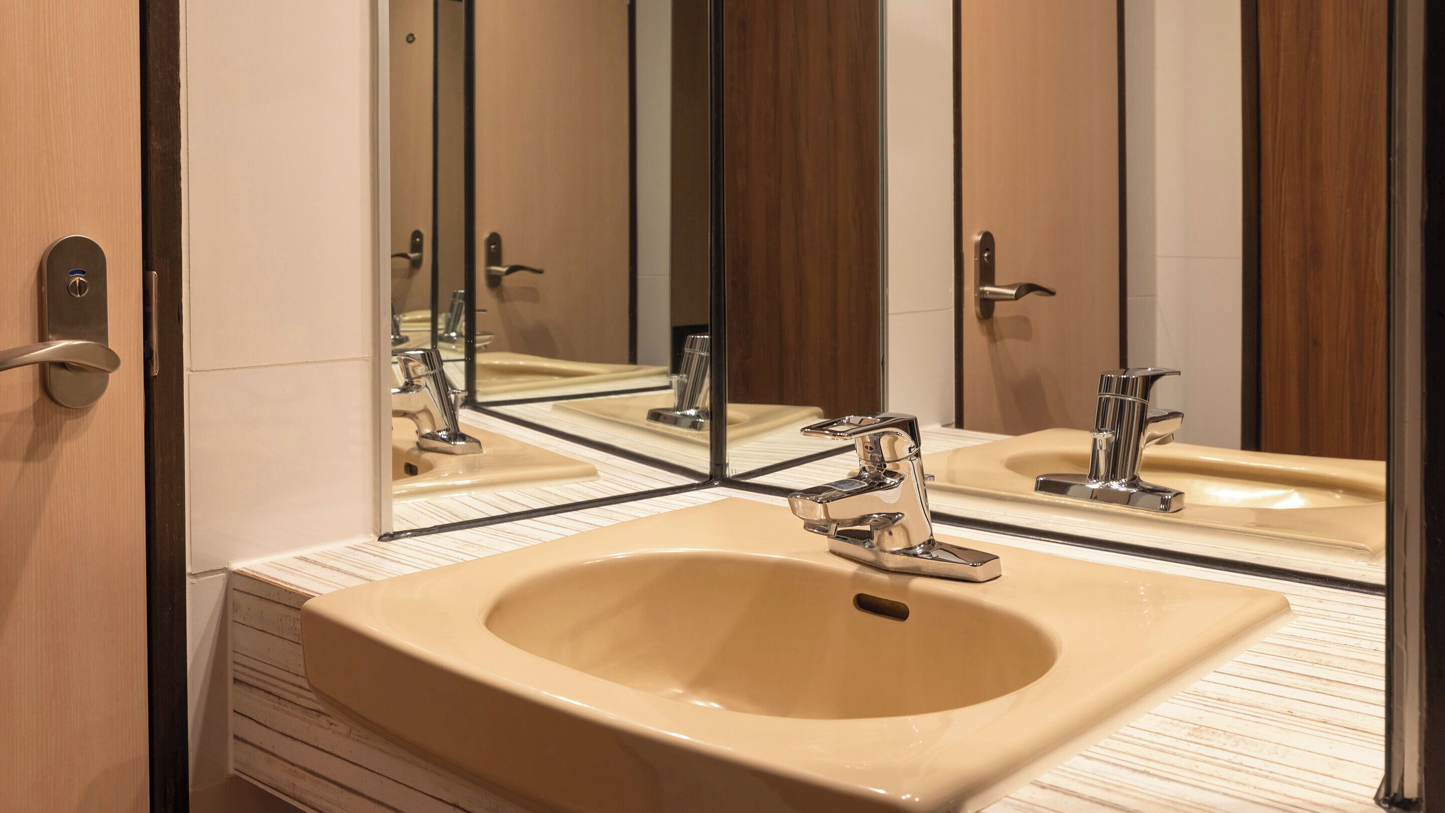 Ein Badezimmer mit einem beigefarbenen Waschbecken, Chromarmaturen und einem Spiegel, der den Raum widerspiegelt.