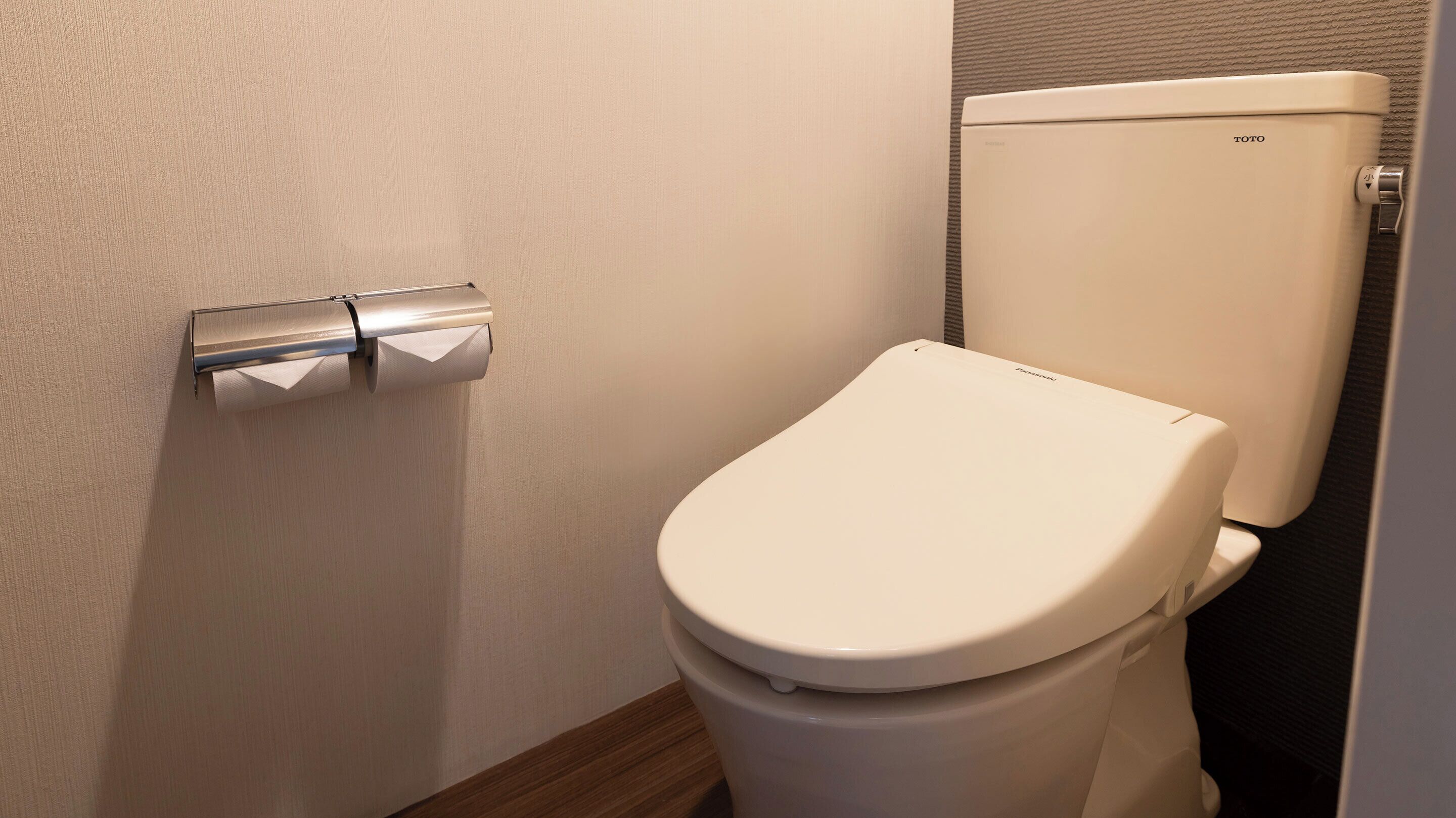 Toilet met een TOTO tank, toiletrolhouder en een houten vloer.